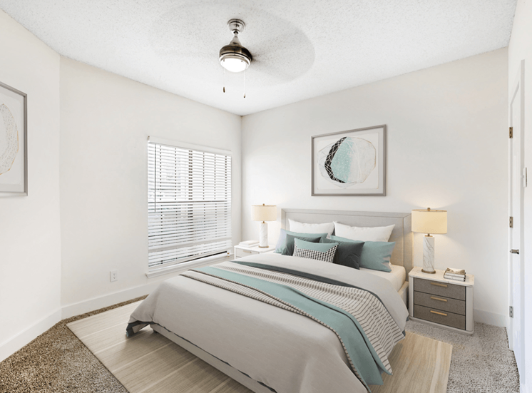 Virtually staged bedroom with carpet, accent rug, bed, nightstands with lamps, ceiling fan with light and large window with blinds